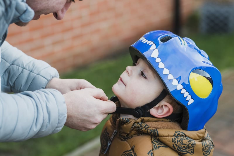 A father fastens his son's safety helmet before going out to play