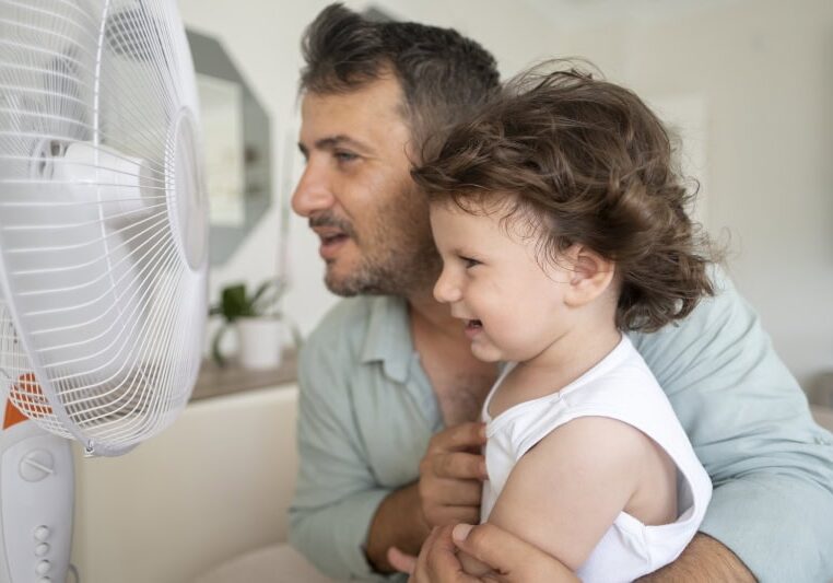 Father child is front of electric fan on hot summer day