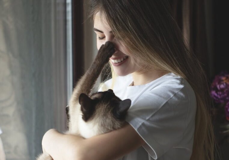 young woman hugging her cat in front of the window.
