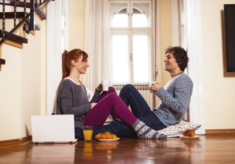 How to Determine Heat Pump Efficiency. Couple sitting on the floor drinking out of mugs and eating breakfast.