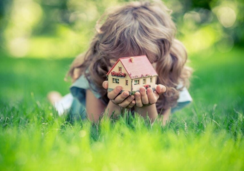 Young girl laying in the grass holding a little toy home.